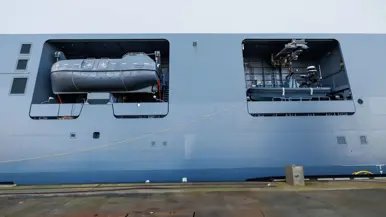 Een grijze kraan op het dek van het schip, een donkergrijze reddingsboot en het predicaat met daarop ‘Den Helder’.