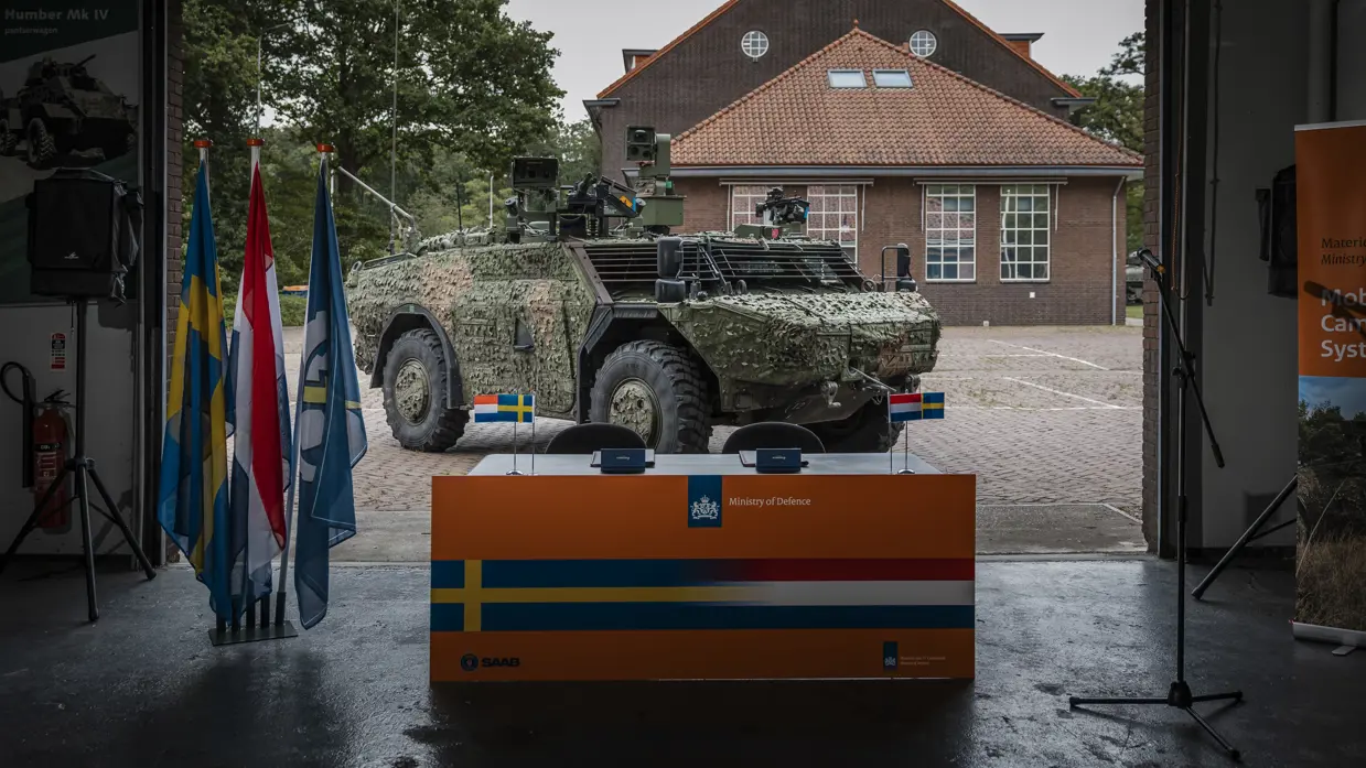  Een officiële tekentafel met daarachter een militair voertuig. 