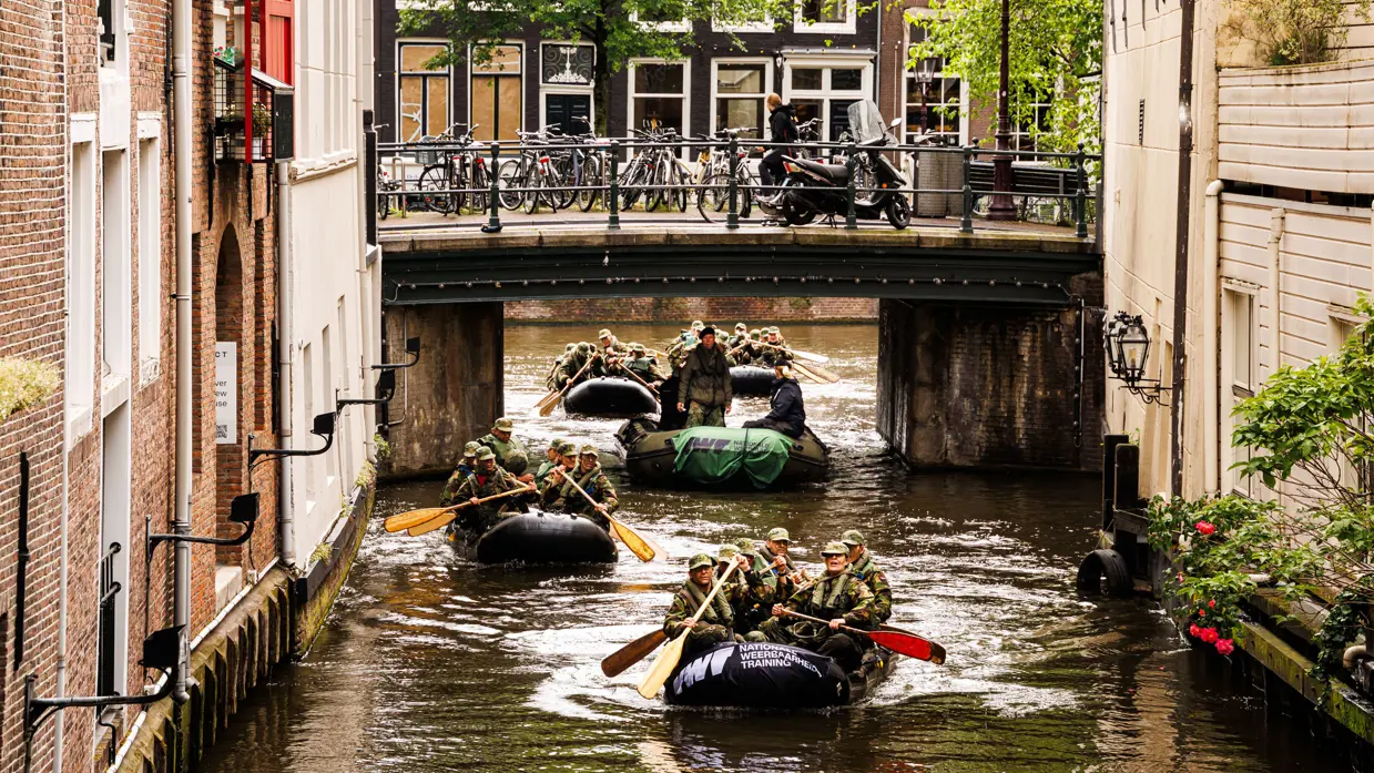 De deelnemers aan de NWT roeien in rubberboten door Amsterdam.