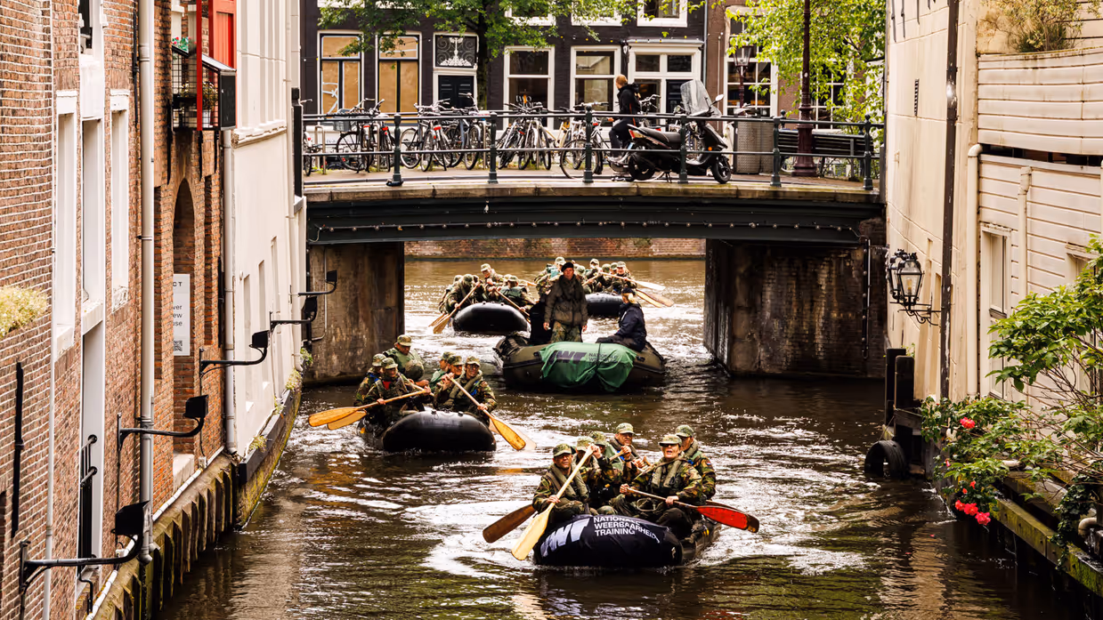 De deelnemers aan de NWT roeien in rubberboten door Amsterdam.