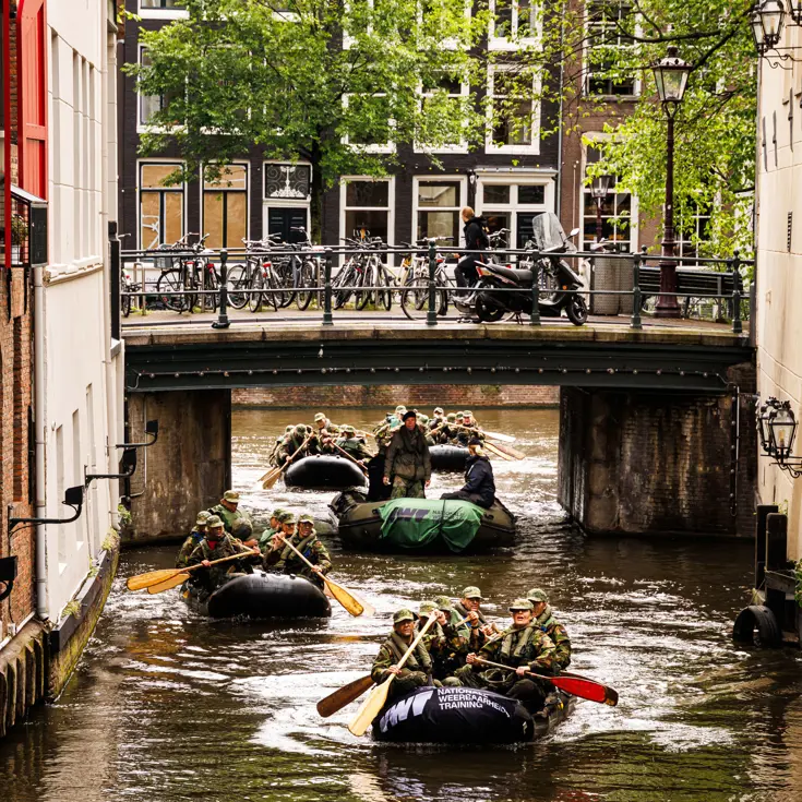 De deelnemers aan de NWT roeien in rubberboten door Amsterdam.