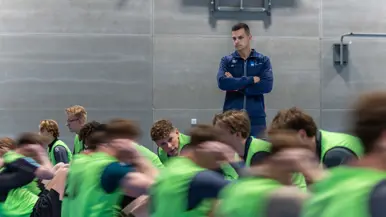 Jongeren in gele hesjes voeren diverse sportonderdelen uit in een sportzaal. 