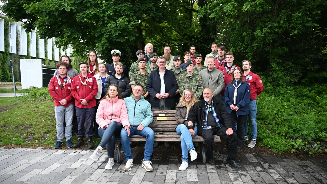 De (stief)ouders van Gijs op het bankje in Emmen met daarachter militairen, de wethouders en scouts. 