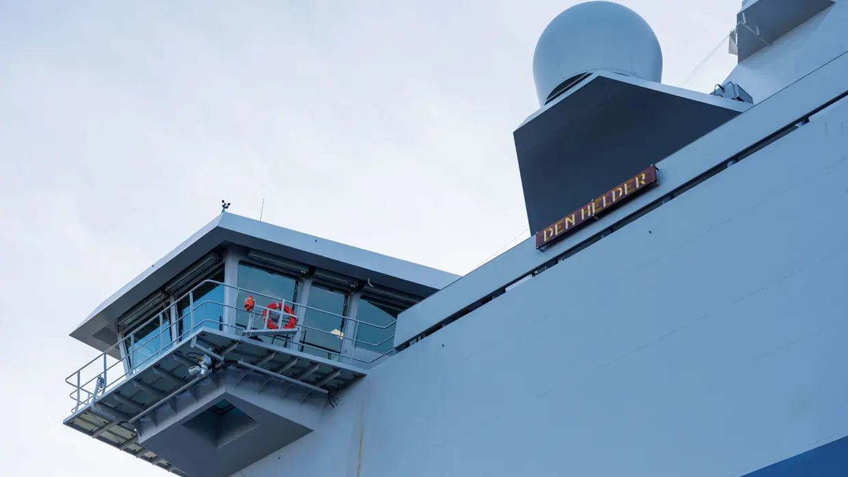 Een grijze kraan op het dek van het schip, een donkergrijze reddingsboot en het predicaat met daarop ‘Den Helder’.