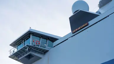 Een grijze kraan op het dek van het schip, een donkergrijze reddingsboot en het predicaat met daarop ‘Den Helder’.