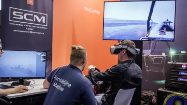 Een persoon in een t-shirt van marine praat in een gameroom tegen iemand in burgerkleding met VR-bril op.