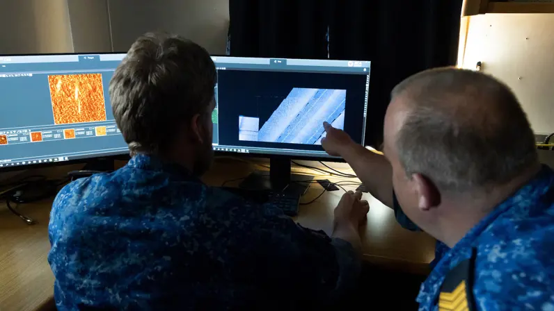 Twee marinecollega’s kijken naar een scherm met onderwaterbeelden. 