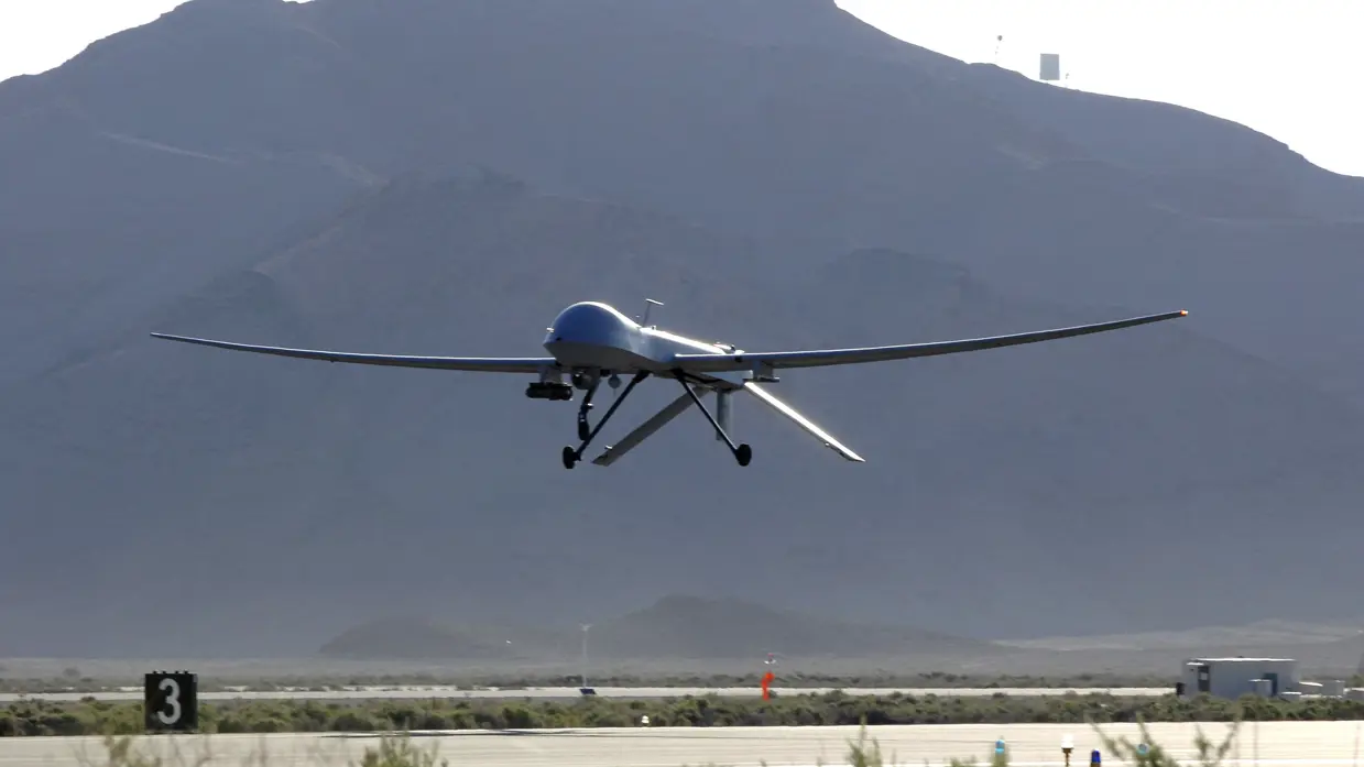 Vlak boven een startbaan vliegende MQ-1. Op de achtergrond een berg.