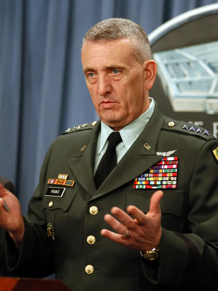 Een man in een groen militair uniform met veel medailles en sterren op zijn borst staat te praten met een ernstige blik. Hij heeft een naamplaatje met daarop ‘Franks’ op zijn uniform.