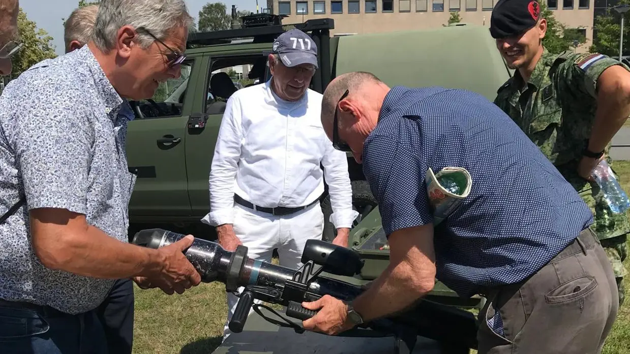  Een militair met een groot wapen wordt omringd door een aantal mensen.