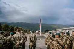 Infanteristen op  de rug gezien met een vlag op de achtergrond en daarachter heuvels.