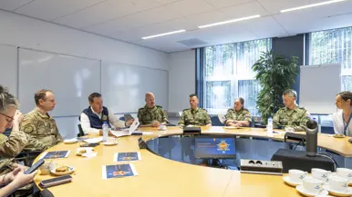 Popolo en Adang samen met nog een aantal militairen en een burger in gesprek aan een ronde tafel.
