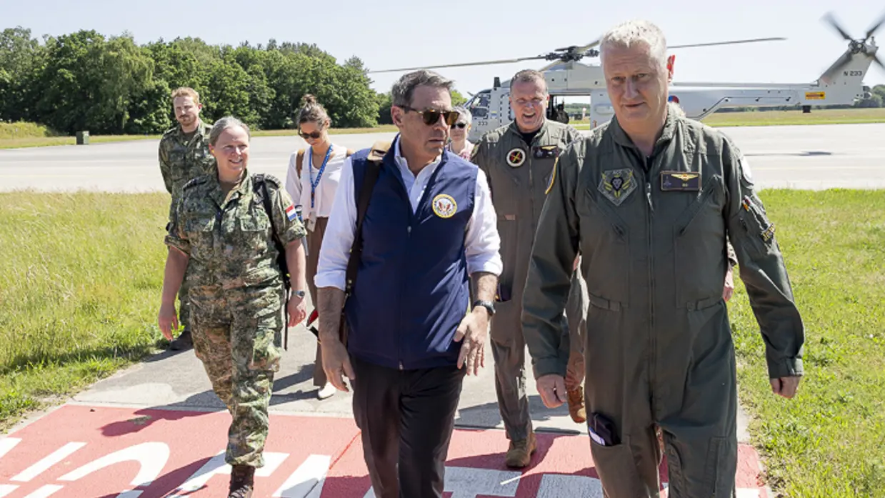 Popolo lopend in gesprek met Commandant Air Combat Command commodore Marcel van Egmond. Achter hen loopt een aantal militairen en burgers met op de achtergrond een NH90. 