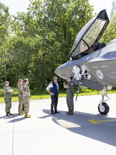 Popolo krijgt naast een F-35 met geopende canopy uitleg van een militair. Op een meter afstand luisteren vier militairen mee.