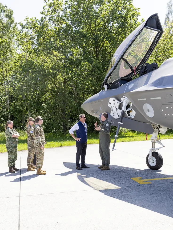 Popolo krijgt naast een F-35 met geopende canopy uitleg van een militair. Op een meter afstand luisteren vier militairen mee.