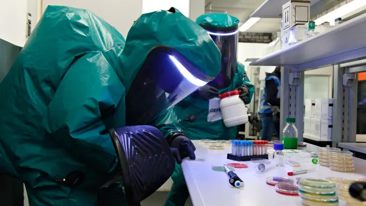 Personen in beschermende pakken onderzoeken petrischaaltjes in een lab.