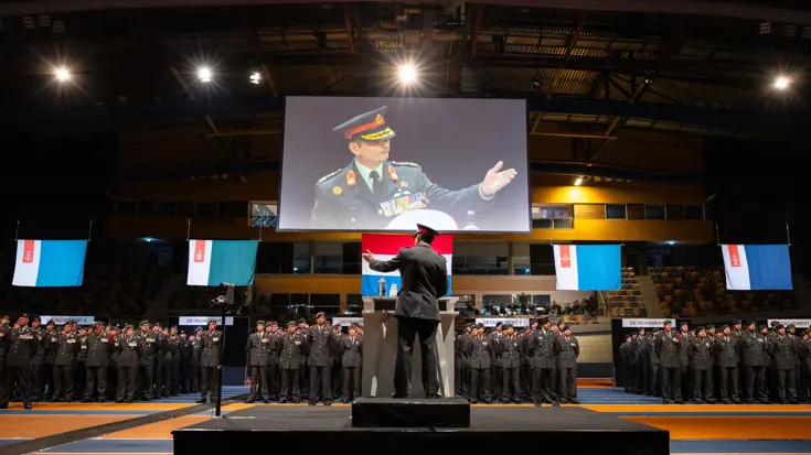 Militair geeft toespraak aan volle zaal met militairen.