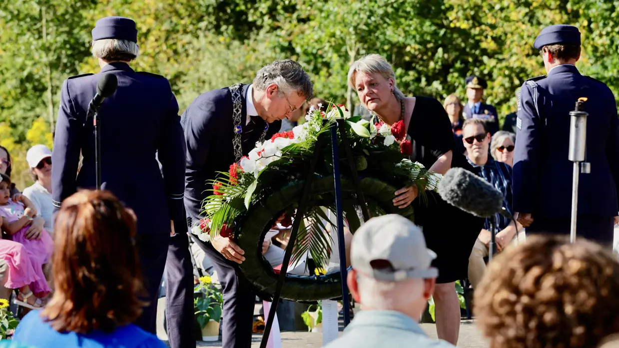 Links en rechts: diverse mensen leggen bloemen bij een kruis met zonnebloemen.