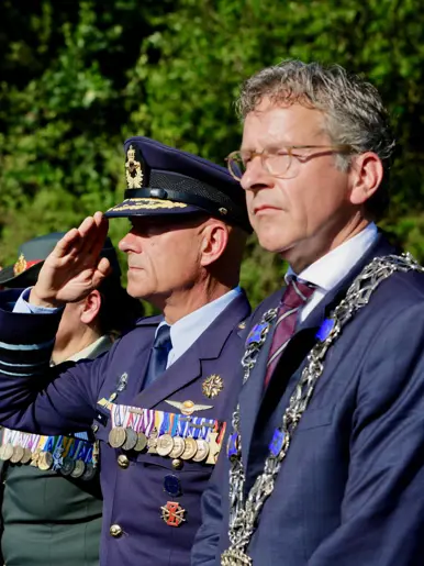 een groep mensen in pak en uniform, waarbij de militairen salueren.