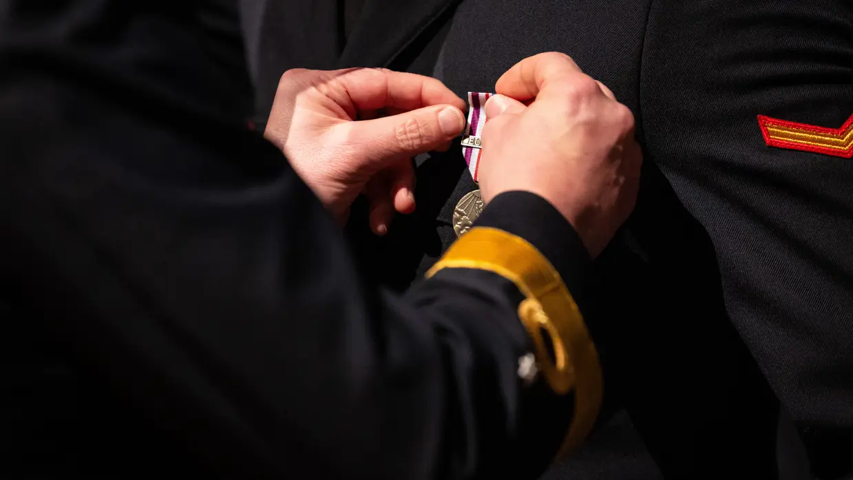 Close up van twee handen die medaille op revers militair spelden.