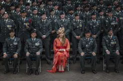 Prinses Amalia in een oranje gewaad zit op een stoel, omringd door landmachtmilitairen in uniform.
