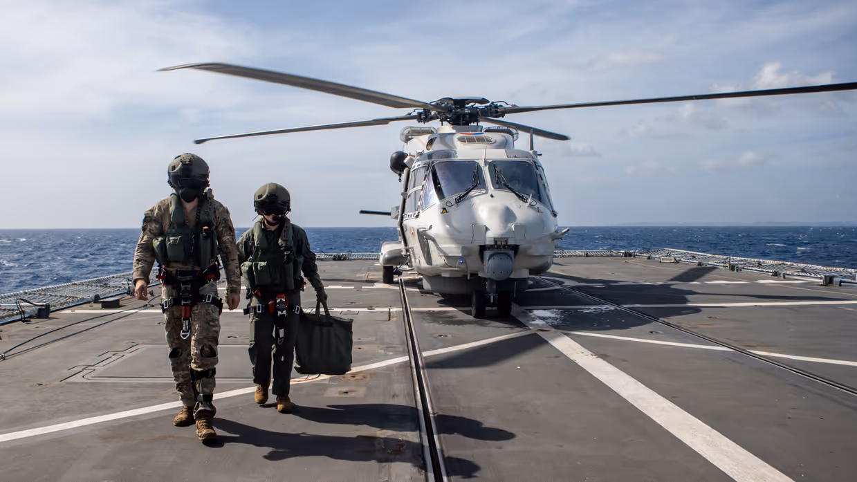 Militairen lopen weg van helikopter geland op dek van schip.