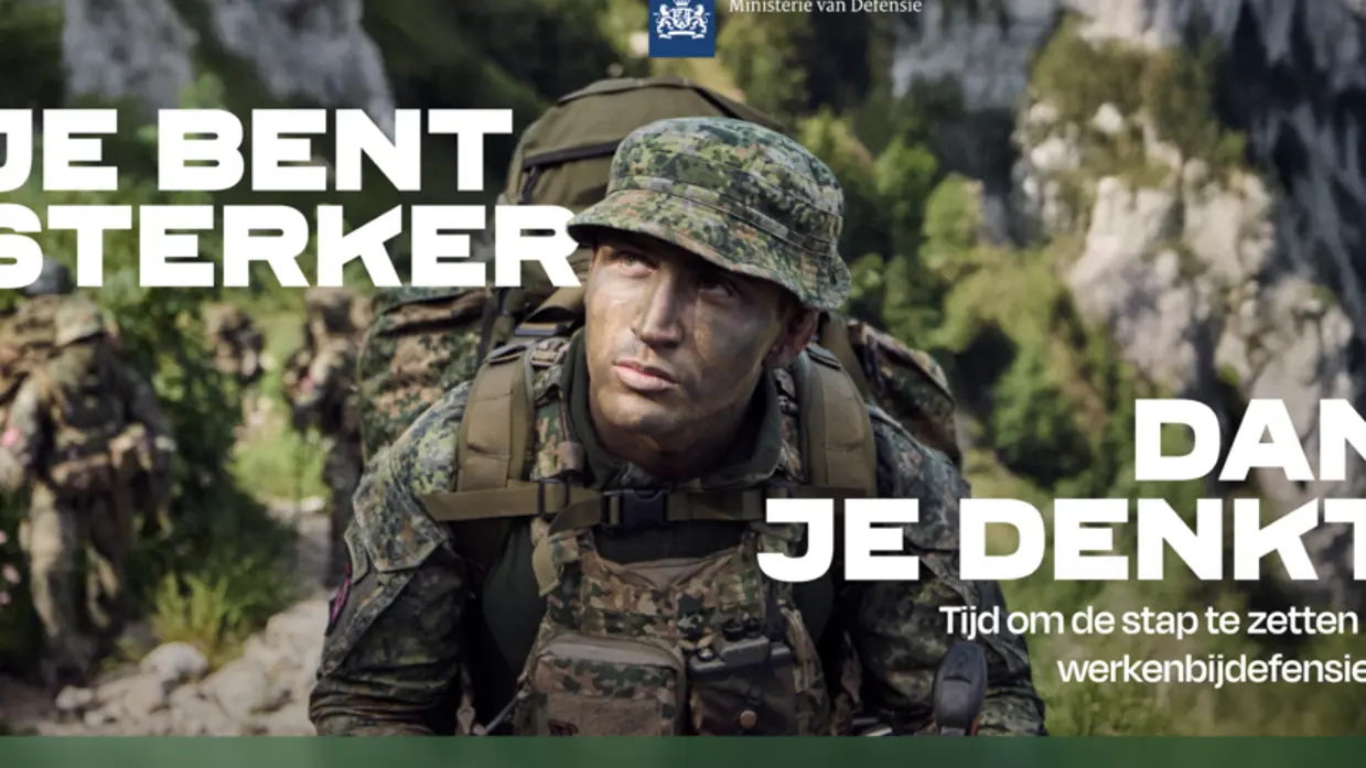 Militair in uniform met groengekleurd gezicht en een slap hoedje op. Op zijn rug een rugzak. Rotsige bergen op de achtergrond.