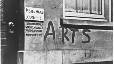 Zwart-wit foto van een muur met "arts" in grote letters en een bordje met spreekuren.