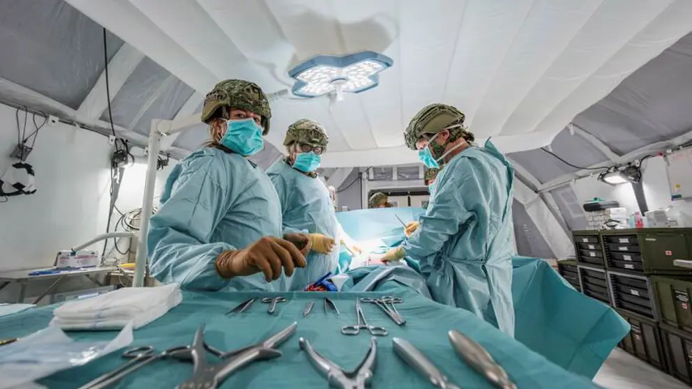 Leden van een chirurgisch team met helmen op en groene pakken aan. Op de voorgrond zilverkleurig medisch gereedschap.