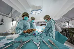 Leden van een chirurgisch team met helmen op en groene pakken aan. Op de voorgrond zilverkleurig medisch gereedschap.