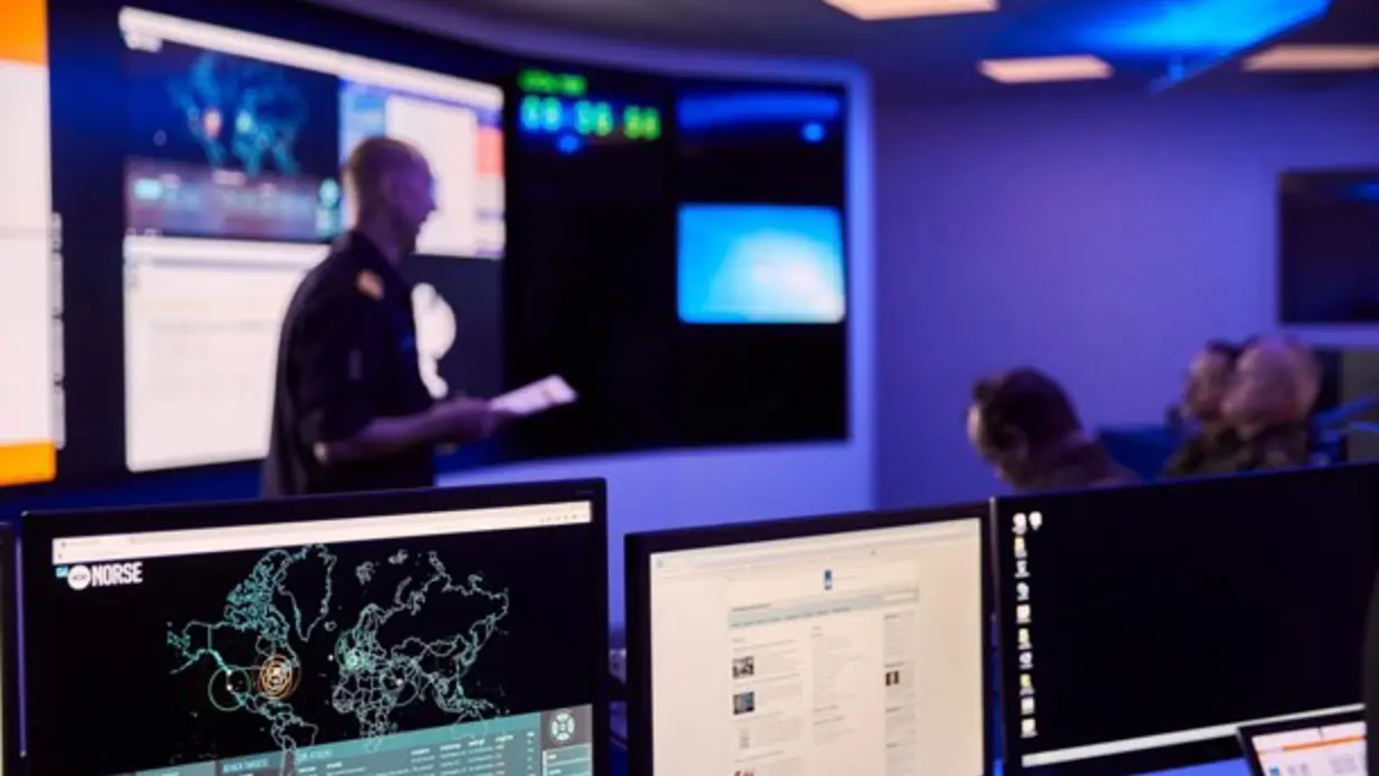 Computers in een donkere ruimte met wazige mensen op de achtergrond.