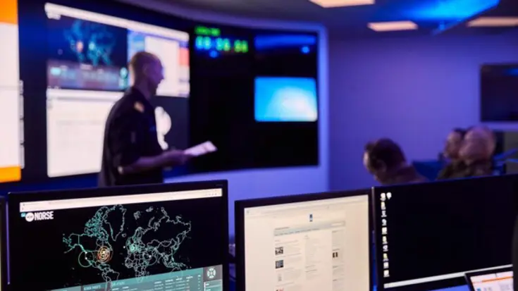 Computers in een donkere ruimte met wazige mensen op de achtergrond.