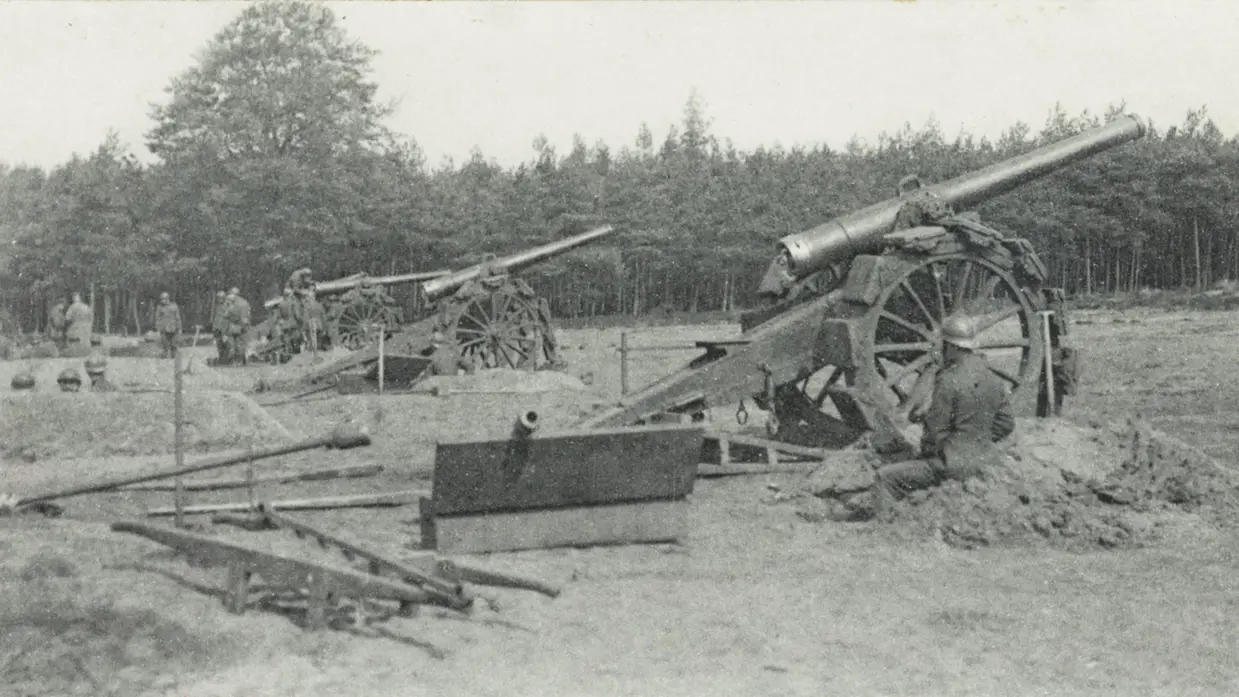 Oude kanonnen op wielen in een open veld, omringd door bomen. Soldaten bedienen de kanonnen, met een rustige, landelijke achtergrond.    