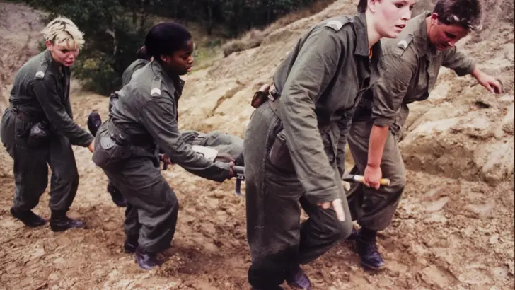 Vrouwelijke korporaals sjouwen oefengewonde op brancard (ca. 1990).
