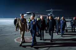 De CDS en minister Brekelmans lopen met een delegatie op een donkere landingsbaan. Op de achtergrond is een vliegtuig te zien.