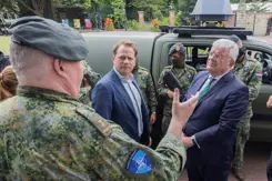 Gijs Tuinman en burgemeester Jan van Zaanen praten buiten met militair. Op de achtergrond voertuig en militairen.