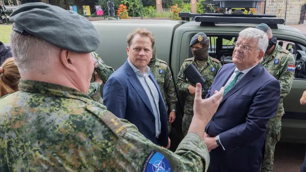 Gijs Tuinman en burgemeester Jan van Zaanen praten buiten met militair. Op de achtergrond voertuig en militairen.