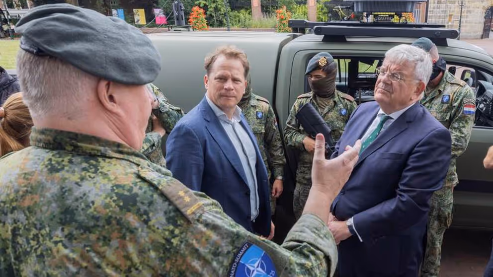 Gijs Tuinman en burgemeester Jan van Zaanen praten buiten met militair. Op de achtergrond voertuig en militairen.