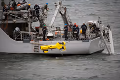 Marineschip waarop militairen een gele onderwaterrobot te water laten.