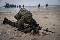 Militair ligt tijdens oefening met wapen gericht op zijn buik op een strand.
