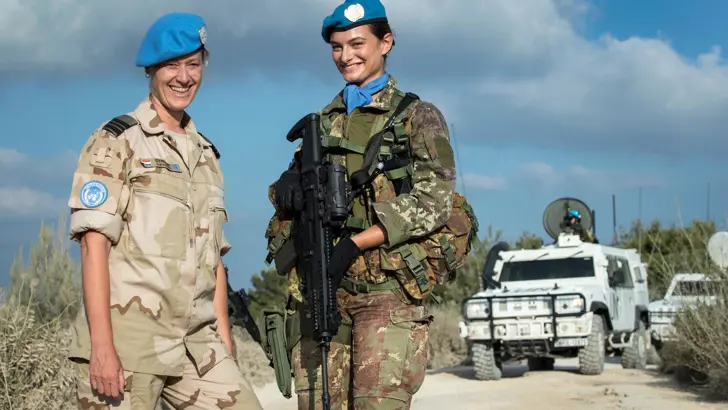 2 vrouwelijke militairen op een zandweg. Eén van hen draagt een geweer.