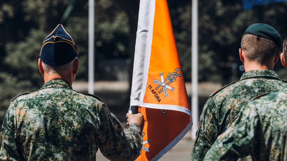 2 militairen met een oranje vaandel tussen hen in.