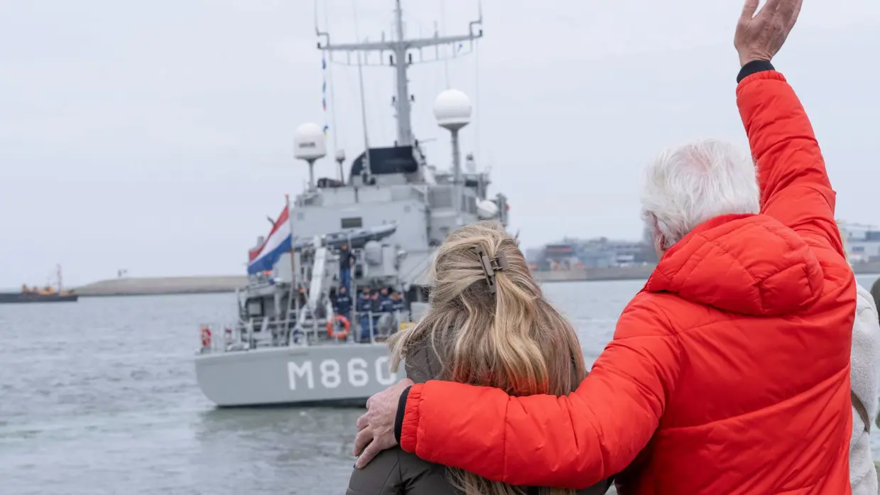 Een man en een vrouw op de kade zwaaien naar de bemanning op het schip. 