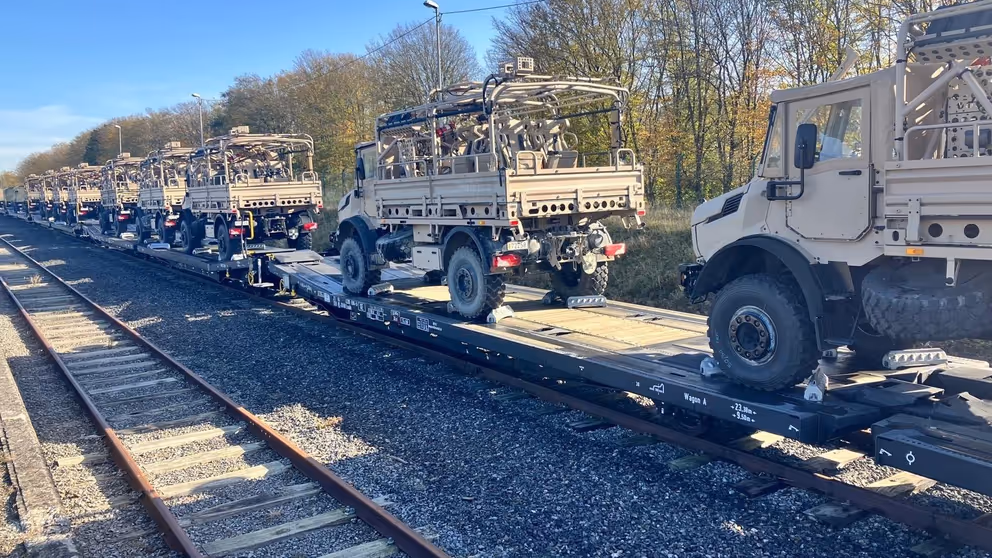 Legervoertuigen staan op treinstel achter elkaar opgesteld om per spoor te worden vervoerd.