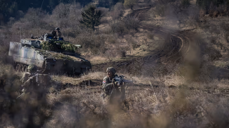 Militair voertuig rijdt door heuvelachtig gebied.