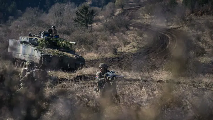 Militair voertuig rijdt door heuvelachtig gebied.