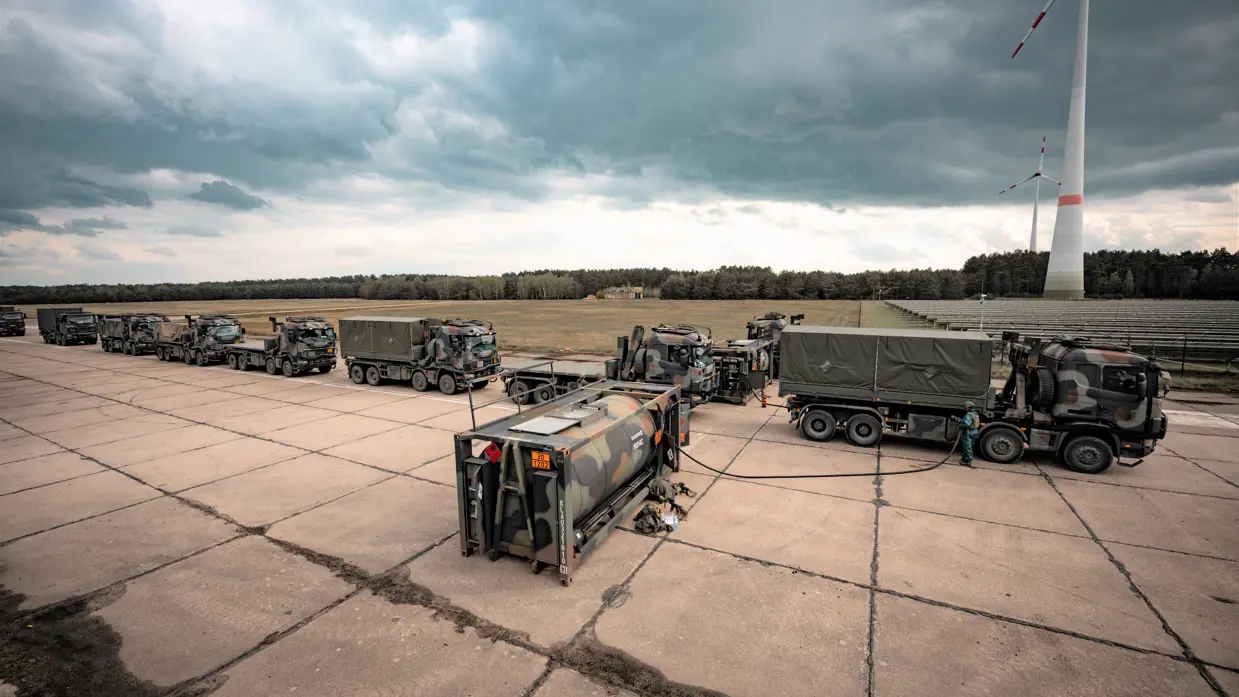 Militaire vrachtwagens staan achter elkaar in een rij om afgetankt te worden.