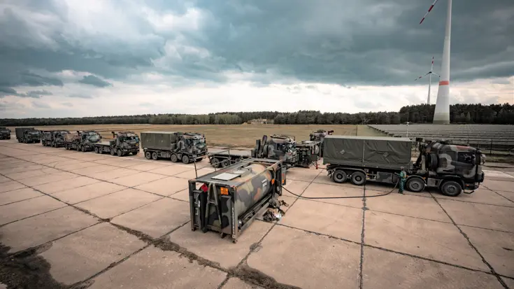 Militaire vrachtwagens staan achter elkaar in een rij om afgetankt te worden.