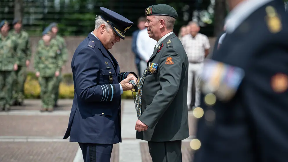 Een militair hangt een andere militair iets om.