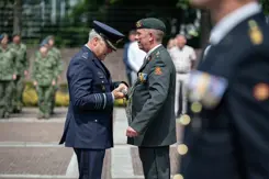 Een militair hangt een andere militair iets om.